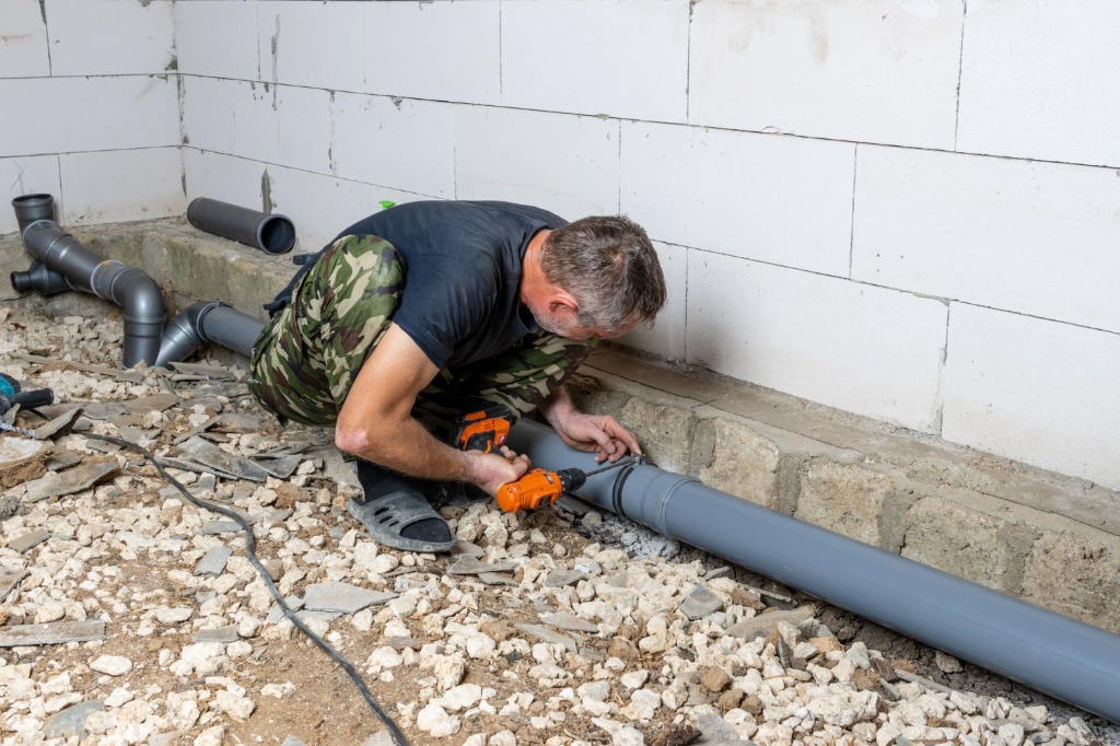 Plumbing technician installing large gray PVC drainage and sewer pipework on site
