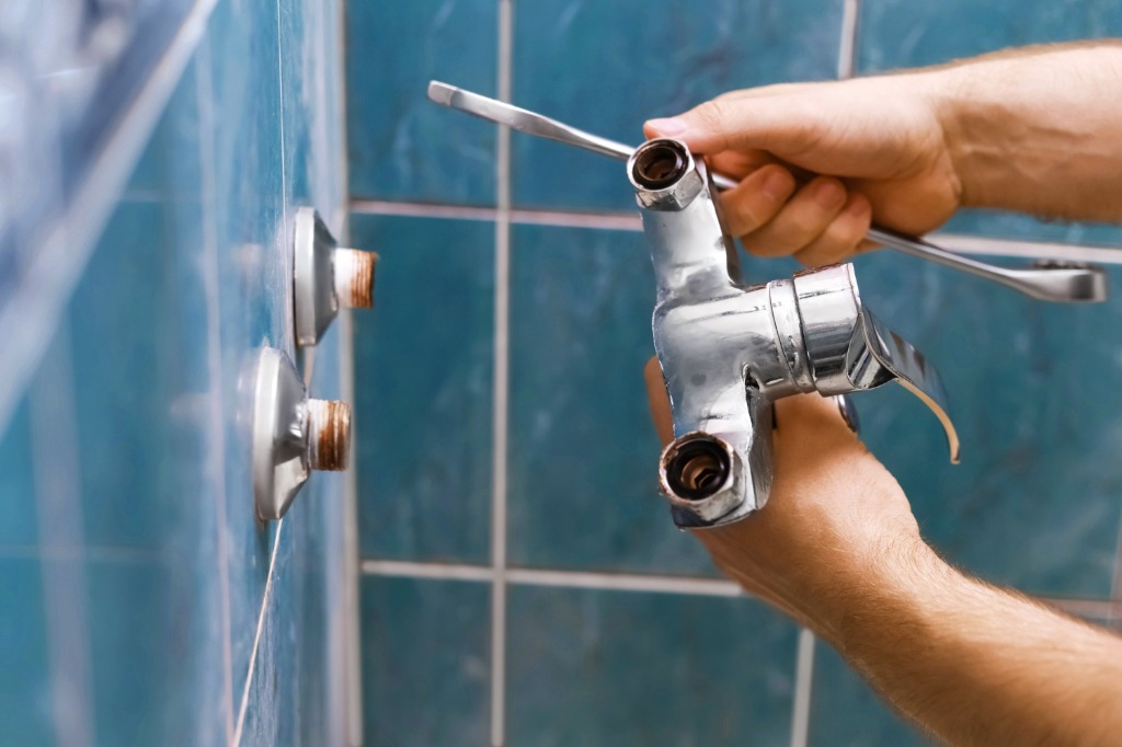 Plumber installing and adjusting chrome bathroom shower mixer tap with wrench in Dubai