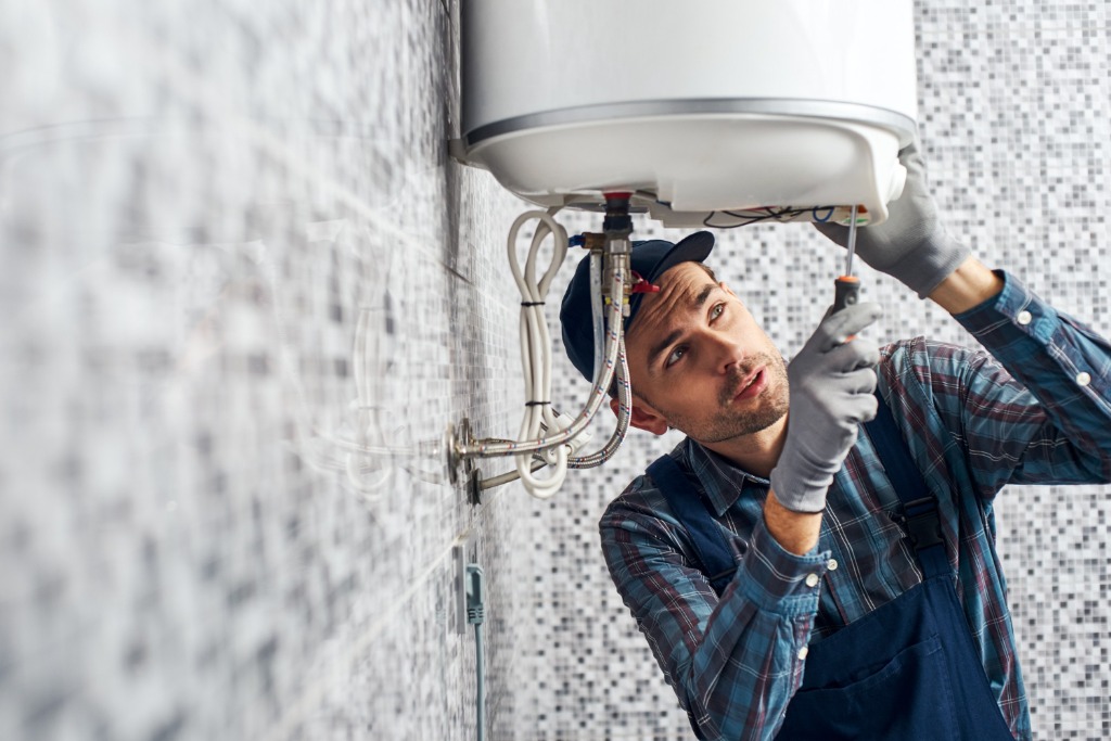 Professional plumber in Dubai repairing electric water heater geyser with screwdriver